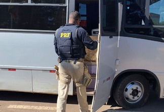 Foto de policial rodoviário federal na porta de micro-ônibus.