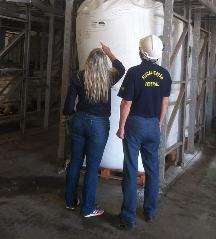 Foto de duas pessoas olhando para um grande saco branco. Uma delas é um fiscal agropecuário.