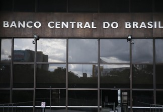 Foto da fachada do Banco Central do Brasil. Ela é espelhada e, acima, está o letreiro.