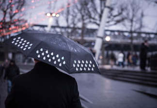 A foto mostra uma pessoas de costas segurando um guarda-chuva preto