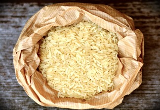 A foto mostra um saco pardo com arroz sem casca.