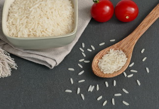 A foto mostra grãos de arroz em uma colher de madeira