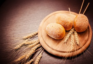 A foto mostra três pães e alguns ramos de trigo