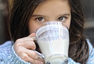 A foto mostra uma criança de cabelo castanho tomando leite.