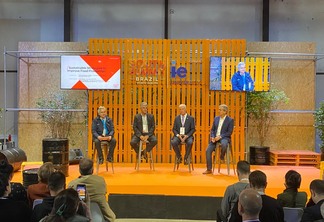 Foto de quatro homens sentados em palco durante evento.