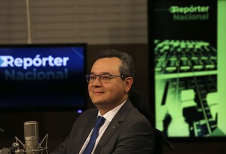 Foto do presidente do Banco do Brasil (BB), Fausto Ribeiro, em um estúdio. Ele está perto de um microfone e usa terno e gravata.