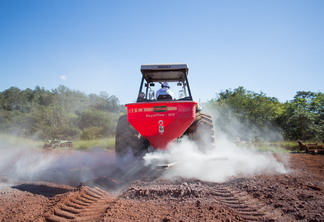 Foto de máquina agrícola vermelha aplicando calcário sobre a terra.