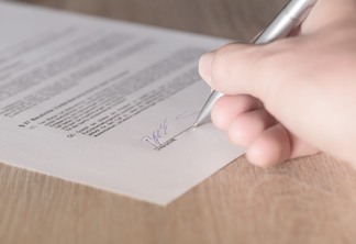 A foto mostra uma mão assinando um contrato