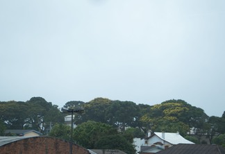 Foto de céu nublado sobre árvores e construções.