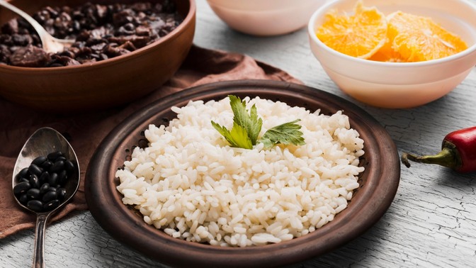 Foto de prato de arroz, ao lado de prato com laranja e com um prato de feijão ao fundo.