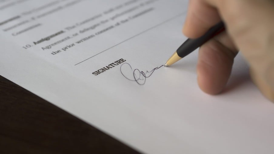 A foto mostra uma mão assinando um contrato
