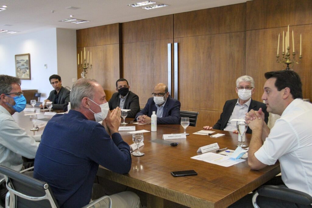 Foto de homens, a maioria com máscaras, durante reunião.
