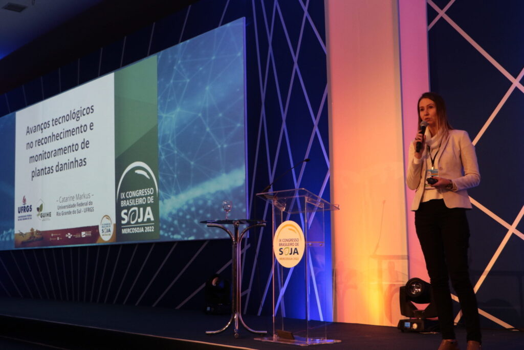 Foto de mulher falando em palco durante palestra.