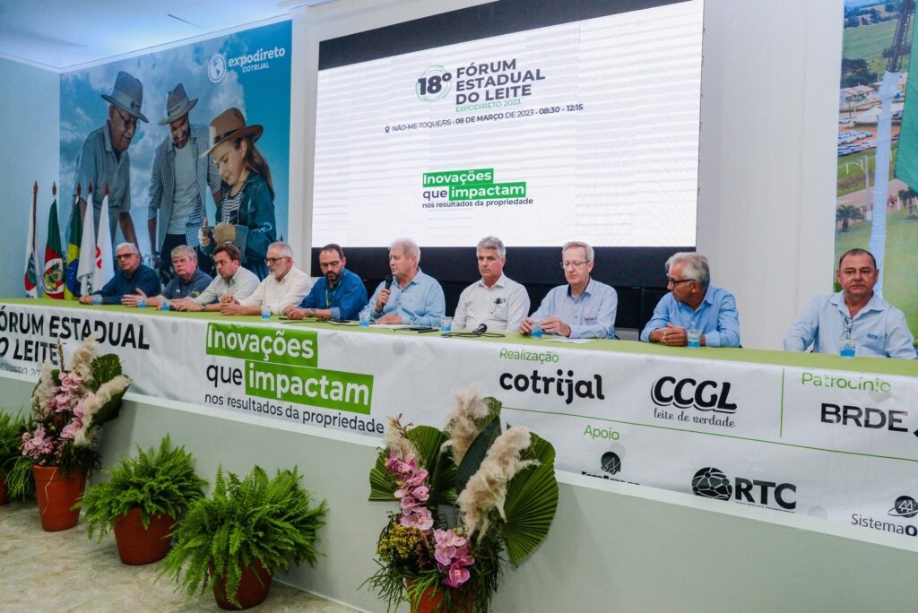 Foto de pessoas sentadas em mesa no palco de um evento.