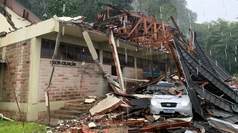 Foto de prédio com parte da cobertura destruída e caída sobre carro.