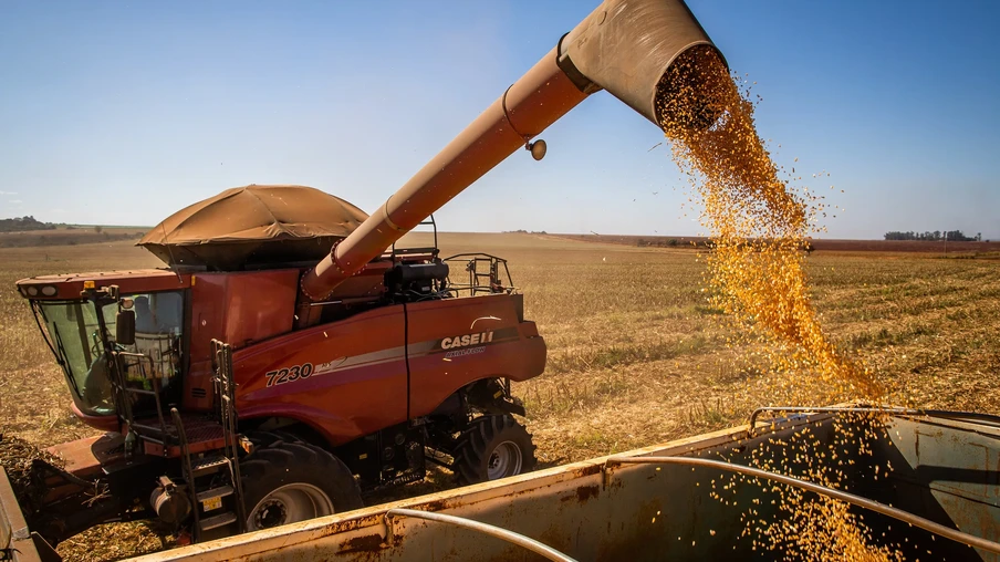 Foto de colheitadeira vermelha despejando grãos de milho em carreta.