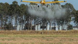 Foto de avião agrícola sobrevoando e realizando a pulverização.