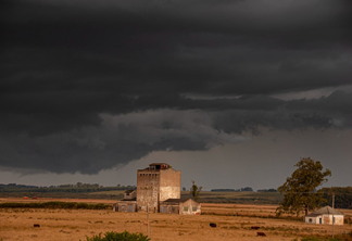 Foto de campo com poucas edificações sob céu escuro. Foto de campo com poucas edificações sob céu escuro.