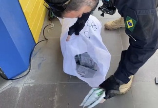 Foto de policial rodoviário federal mexendo em saco com pacotes de agrotóxicos.
