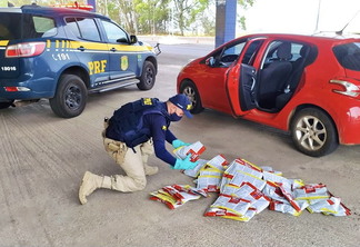 Foto de policial rodoviário federal mexendo em embalagens de agrotóxicos que estão no chão.
