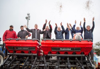 Foto de pessoas em cima de máquina agrícola jogando sementes para o alto.