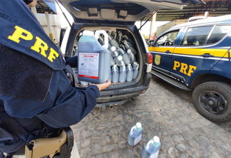 Foto de policial rodoviário federal segurando galão próximo a carro com galões de agrotóxicos.