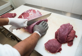 Foto de mão com luvas cortando pedaços de carne.