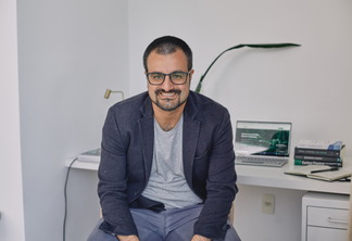 Foto de Luis Felipe Adaime. Ele está em um escritório, sentado e de costas para uma mesa. Ele é branco, usa óculos e tem cabelo ralo. Ele sorri para a foto.