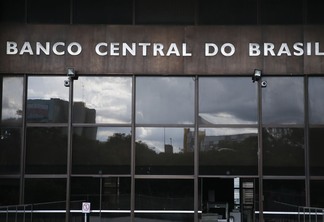 Foto da fachada do Banco Central do Brasil. Ela é espelhada e, acima, está o letreiro. Foto da fachada do Banco Central do Brasil. Ela é espelhada e, acima, está o letreiro.