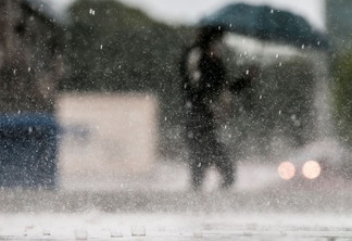 Foto de pessoa com guarda-chuva em meio a chuva forte. A foto foca nos pingos de chuva.