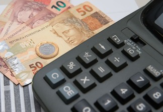 Foto de calculadora com notas e moeda de real ao lado.