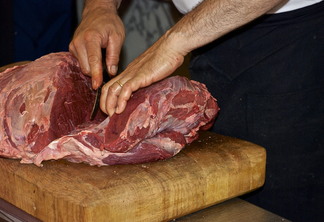 Na foto aparece as mãos de um homem cortando um pedaço de carne bovina Na foto aparece as mãos de um homem cortando um pedaço de carne bovina