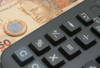 Foto de notas de real e uma moeda ao lado de calculadora.