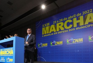 Foto de Jair Bolsonaro em púlpito durante discurso. Ele está no palco da 23ª Marcha a Brasília em Defesa dos Municípios.