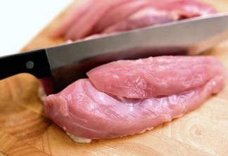 Foto de faca cortando pedaço de carne de frango crua.