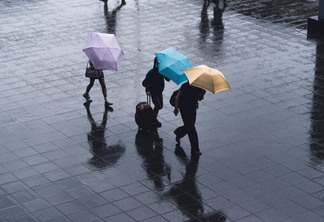 A foto mostra pessoas com guarda-chuvas coloridos em uma calçada