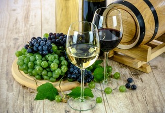 A foto mostra duas taças de vinho e uvas no fundo