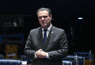Foto de Carlos Fávaro durante pronunciamento no Plenário do Senado. Ele é branco, tem cabelo castanho escuro grisalho, usa terno preto e gravata azul. Está com as duas mãos juntas em frente ao corpo enquanto fala.