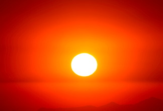 Foto de sol em meio a céu avermelhado.