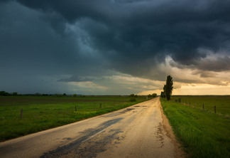 A foto mostra nuvens de chuva sobre uma estrada que divide dois campos verdes