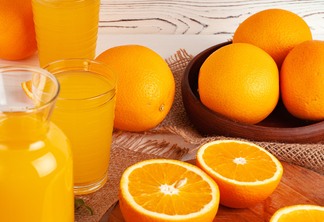 Copo de suco de laranja e laranjas cortadas na mesa.