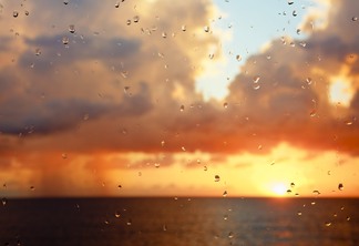 A foto mostra o mar e nuvens alaranjadas com o nascer ou pôr-do-sol