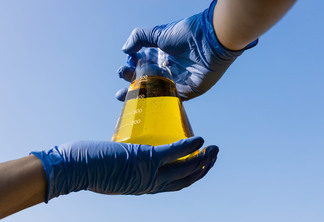 Mão com luvas segurando o copo com biocombustível etanol contra o céu azul