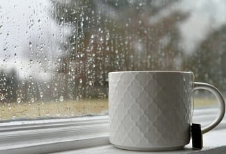 Caneca branca de chá com um saquinho de chá no parapeito da janela por janela coberto de gotas de chuva em um dia frio e chuvoso