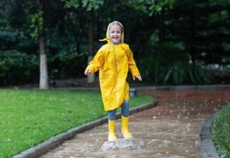 Criança com capa de chuva amarela andando em uma rua enquanto chove.