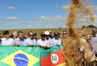 A foto mostra algumas pessoas segurando a bandeira do Rio Grande do Sul e do Brasil, e com soja caindo
