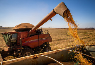 Foto de colheitadeira despejando grãos em caminhão.