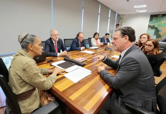 Foto com a ministra Marina Silva sentada na ponta de uma mesa de reuniões. Ao lado dela está o ministro Carlos Fávaro e outras pessoas estão sentadas ao redor da mesa.