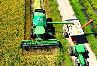 Foto de colheitadeira em lavoura de arroz despejando grãos em carreta graneleira.