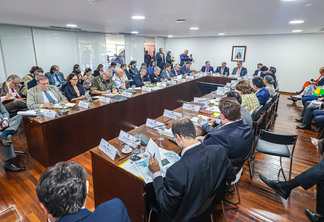 Foto de Reunião na sala de situação sobre as chuvas no Rio Grande do Sul, no Palácio do Planalto. Muitas pessoas estão sentadas ao redor de mesa enquanto conversam e analisam papéis.